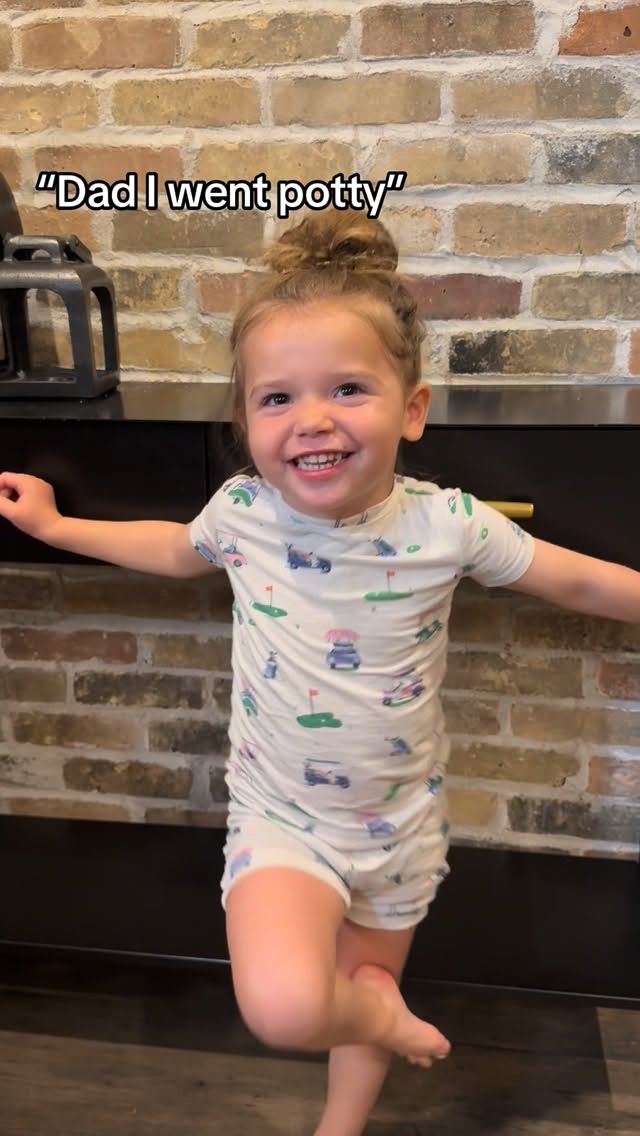 A smiling toddler in front of a brick fireplace, from the May reel.